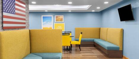 A modern interior with yellow and teal seating, a brick wall, and a mounted TV.