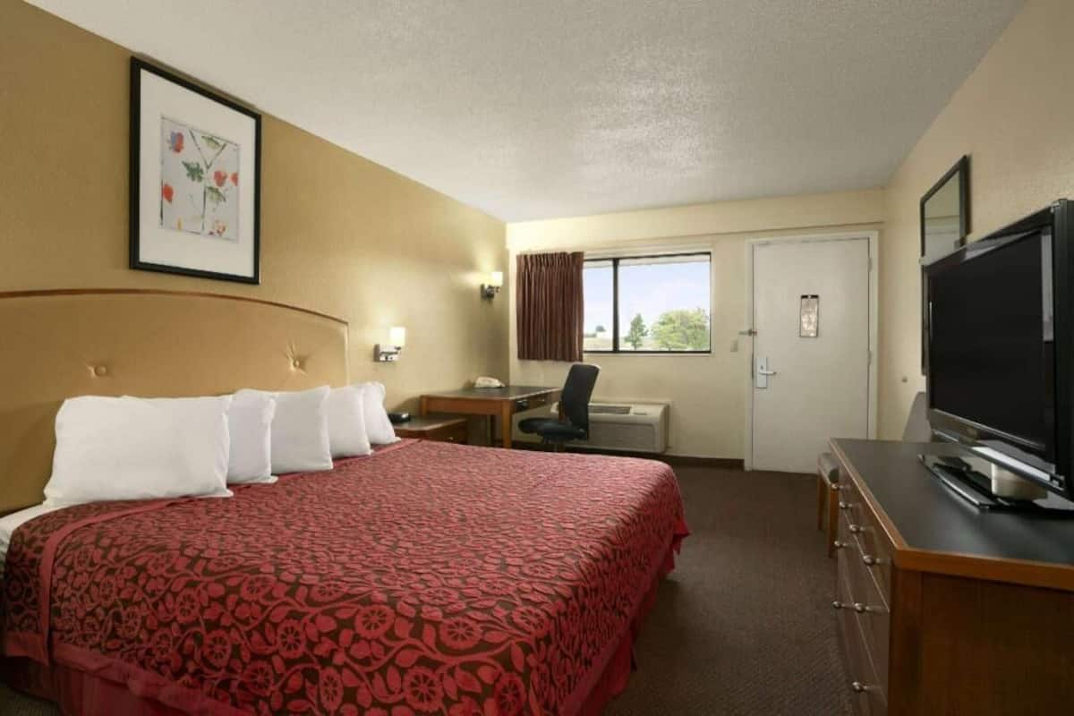 A hotel room with a large bed, a desk, a chair, a television, and a window with curtains.
