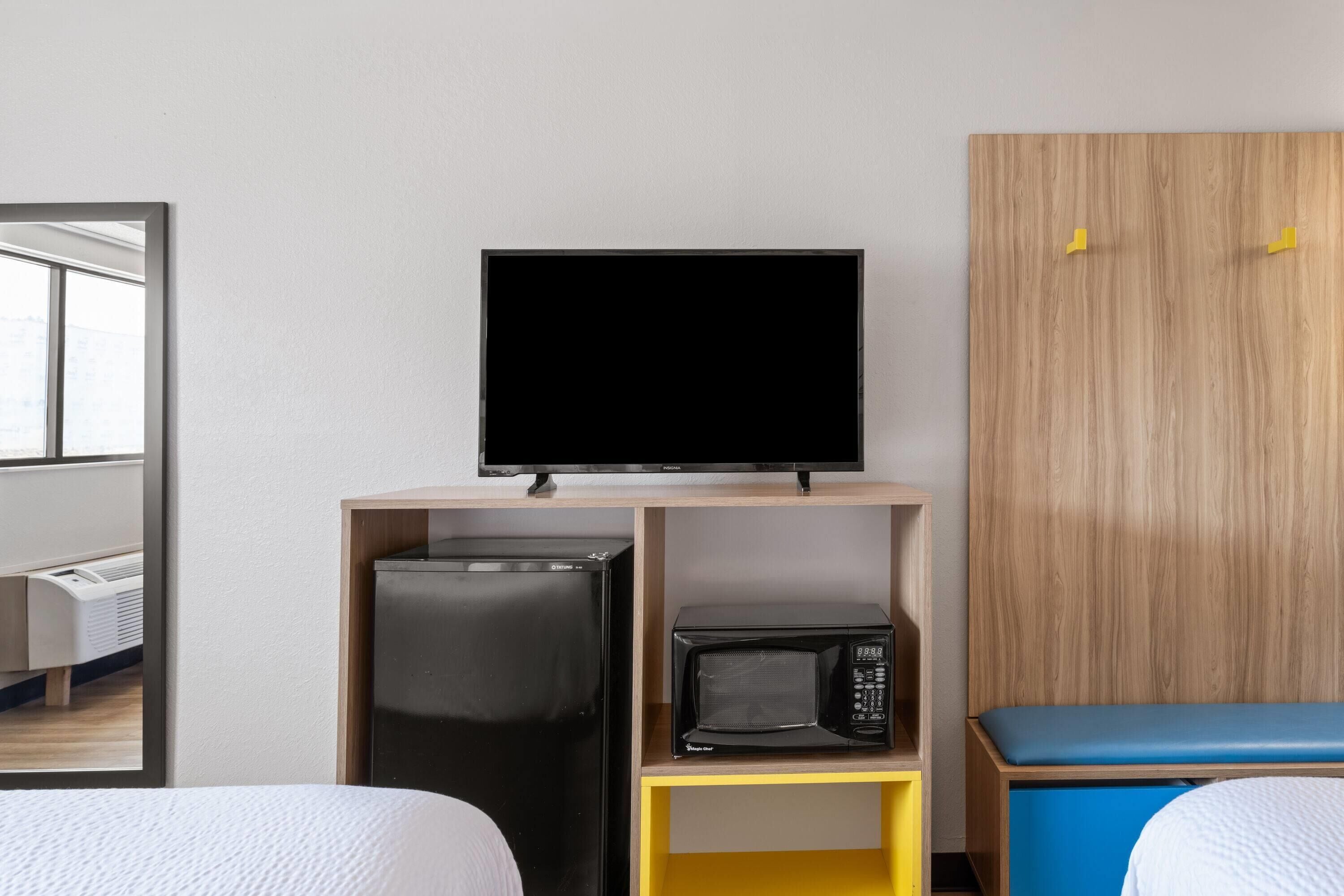Une chambre d’hôtel avec un lit, un téléviseur posé sur une étagère, un réfrigérateur, un four à micro-ondes et une armoire en bois.