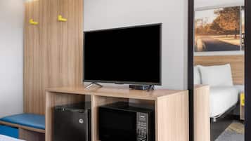 Quarto de hotel com escrivaninha de madeira, televisão, micro-ondas e cama com vista para um parque.