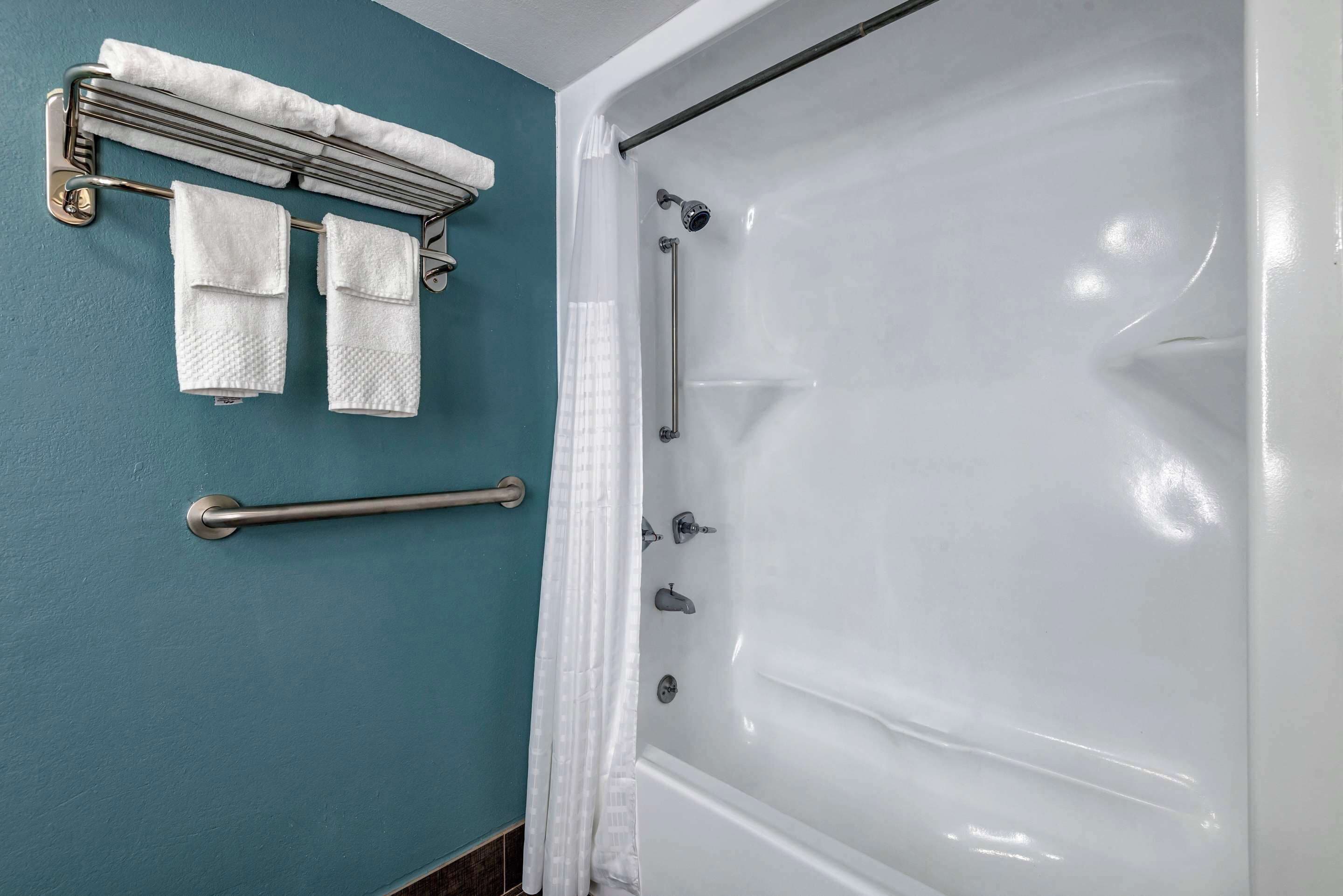 A bathroom with a bathtub, a towel rack with towels, and a grab bar.