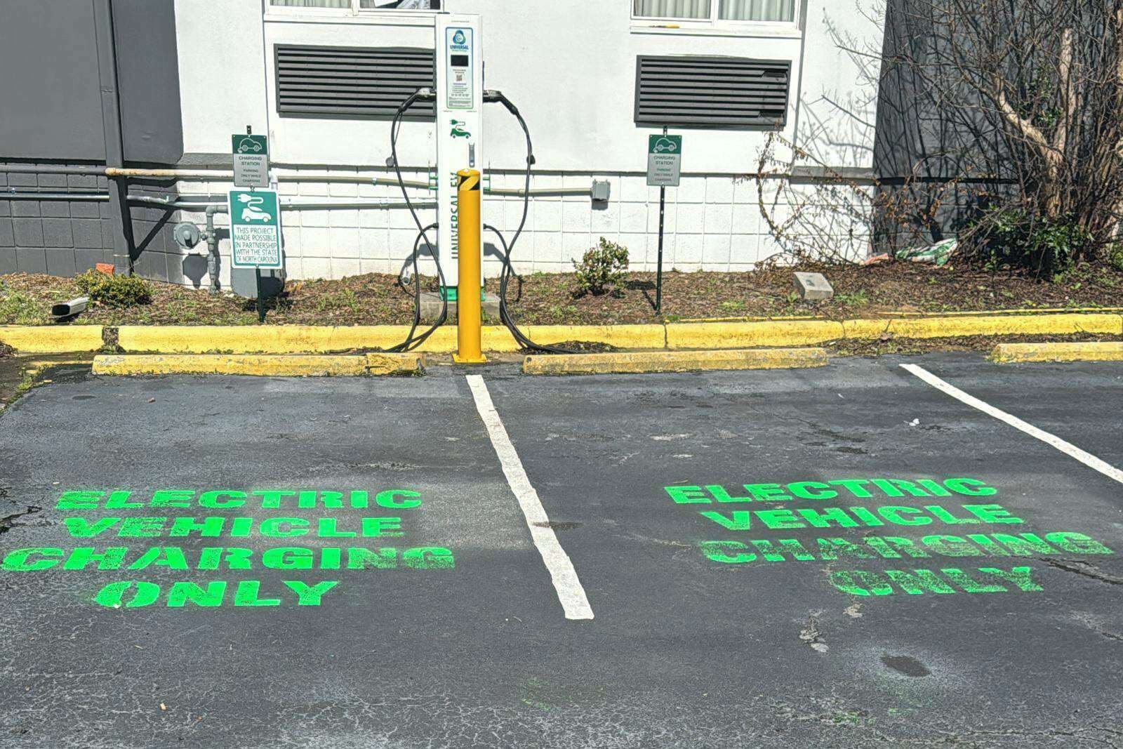 A parking area marked for electric vehicle charging, with a yellow bollard and charging station.