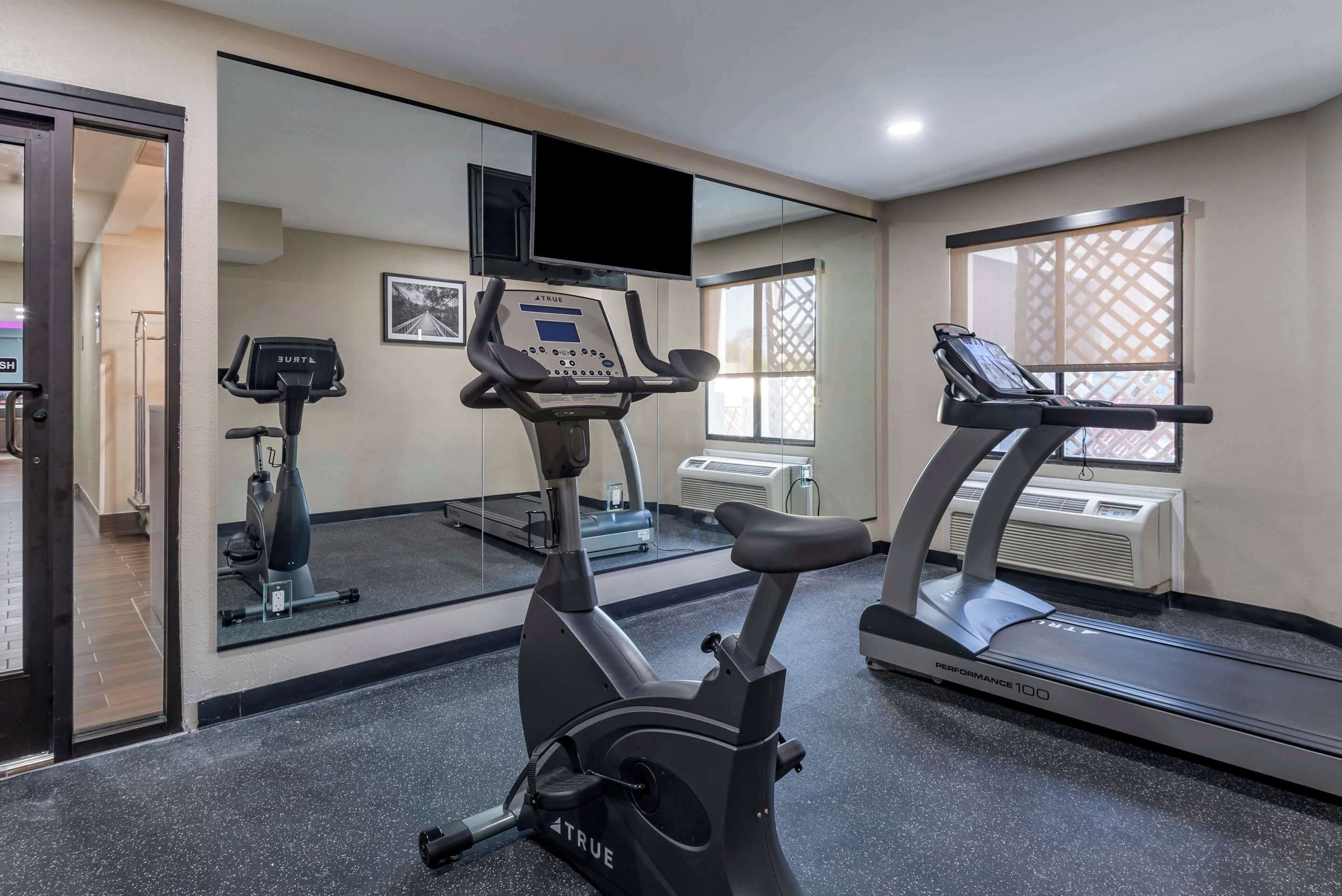 A gym with exercise equipment, a treadmill, an elliptical, and a mirrored wall.