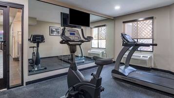 A gym with exercise equipment, a treadmill, an elliptical, and a mirrored wall.