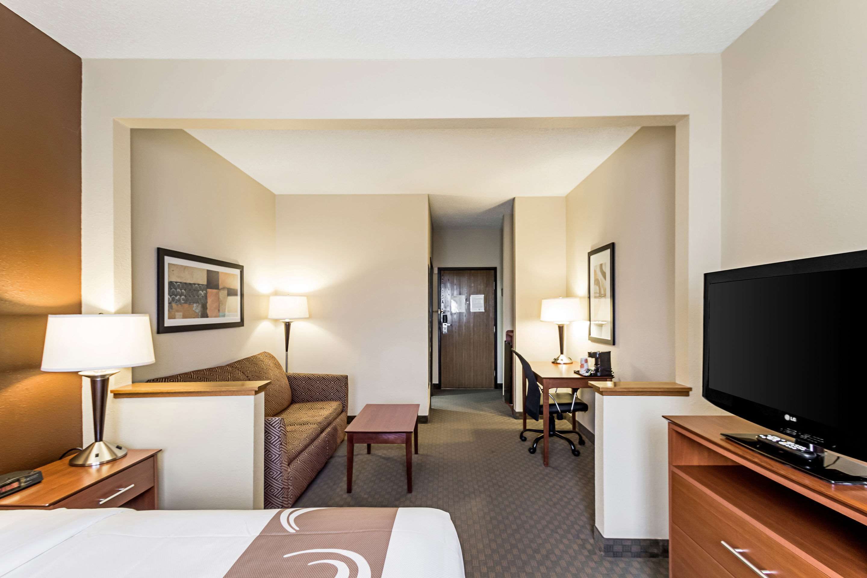 A hotel room with a bed, a desk, a television, and a seating area with a couch and chairs.