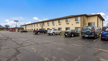 A parking lot with several cars and a hotel building with multiple windows and a sign.