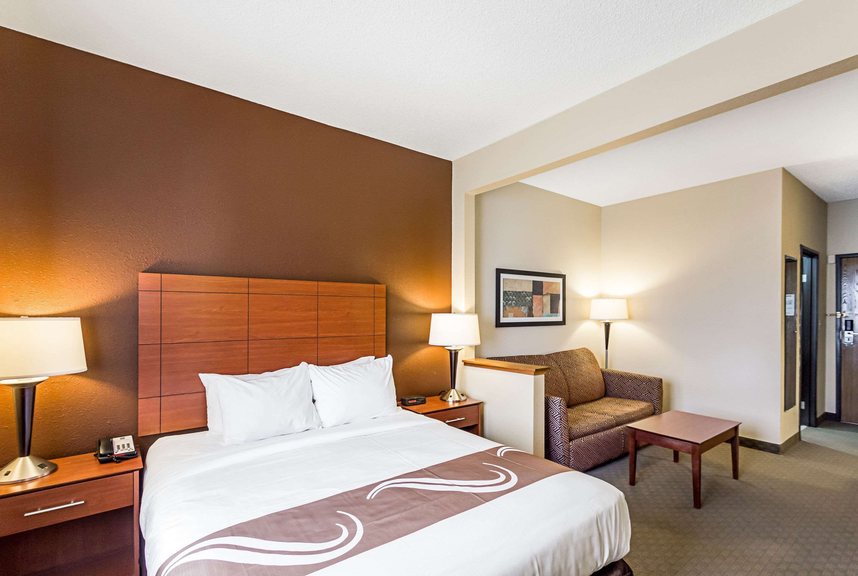 A hotel room with a large bed, two bedside tables, a chair, and a small table.