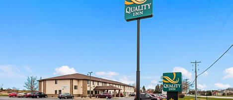 A Quality Inn hotel with a large sign, a parking lot, and a building with a brown roof.