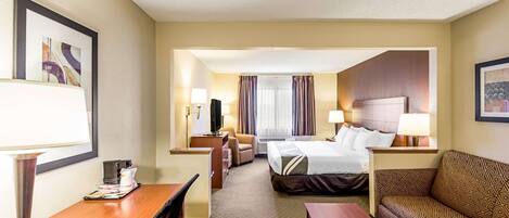 Une chambre d’hôtel avec un lit, un canapé, un bureau et une chaise. Il y a une fenêtre avec des rideaux, une télévision et une lampe sur le bureau.