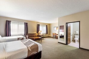 A hotel room with two beds, a sofa, a desk, and a bathroom.