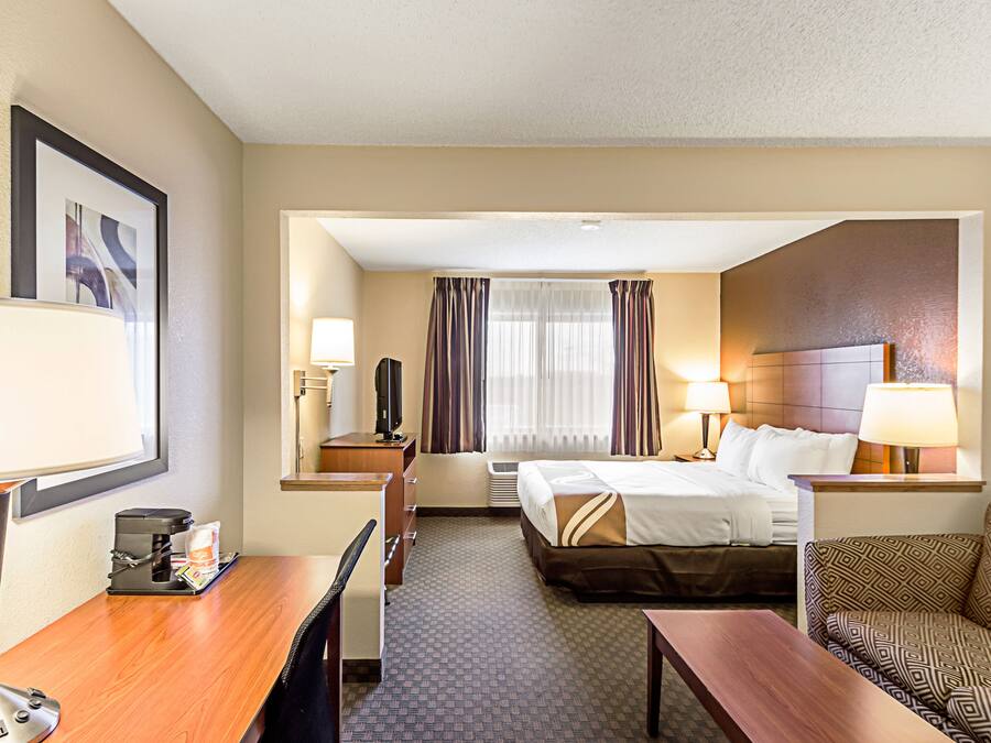 A hotel room with a bed, a desk, a chair, a TV, and a window with curtains.