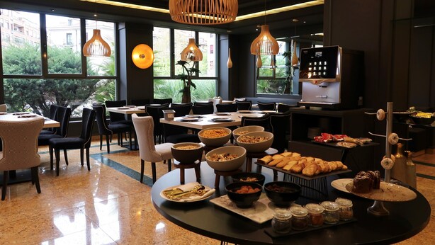 A dining area with round tables, chairs, and a buffet setup with various food items. - Hotel Olid (Valladolid)