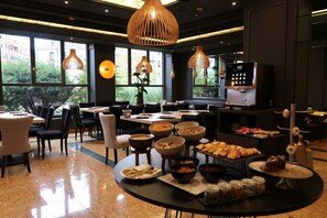 A dining area with round tables, chairs, and a buffet setup with various food items. - Hotel Olid (Valladolid)