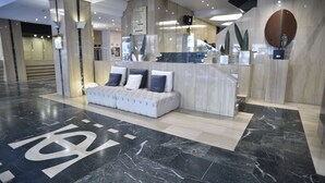 A modern lobby with a reception desk, a seating area with a sofa and pillows, and a marble floor with a large 'K' logo. - Hotel Olid (Valladolid)