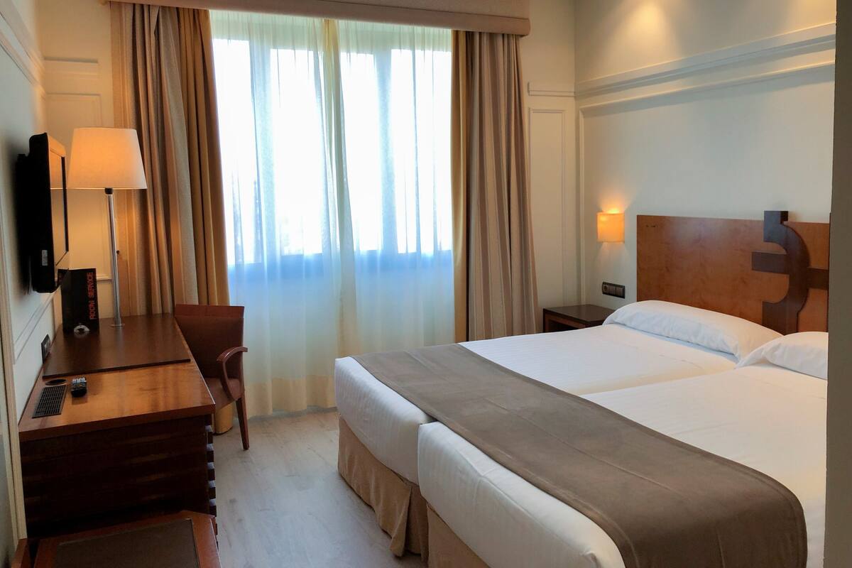 Habitación de hotel con cama, mesitas de noche, escritorio, silla y televisión.