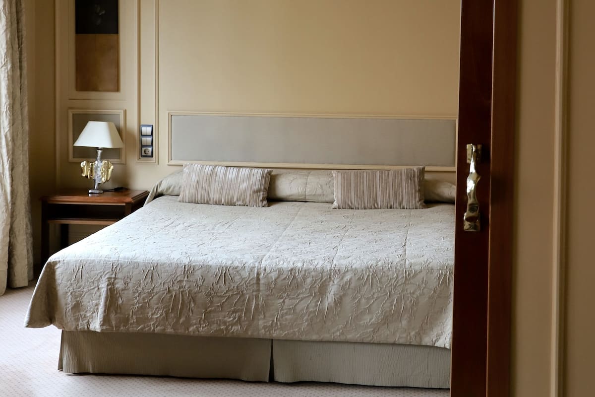 Una habitación de hotel con una cama grande, una mesita de noche con lámpara y un armario.