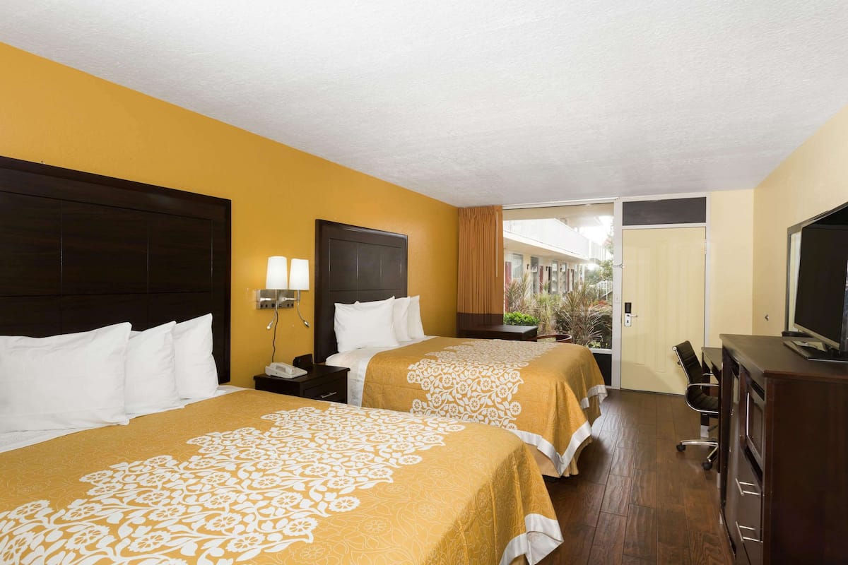 A hotel room with two beds, a desk, a television, and a view of the outside.