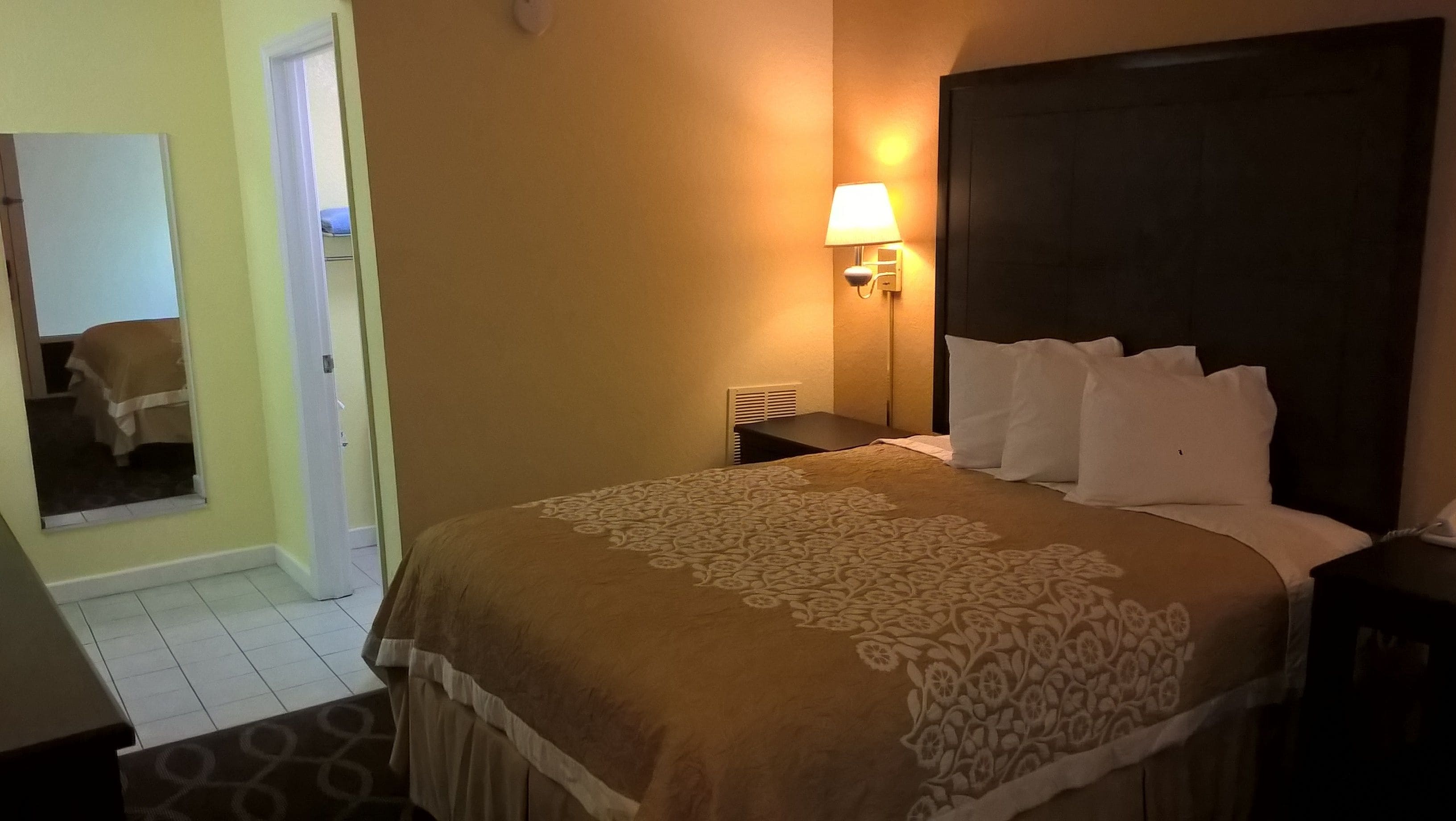 A hotel room with a bed, a bedside table, a lamp, and a mirror.