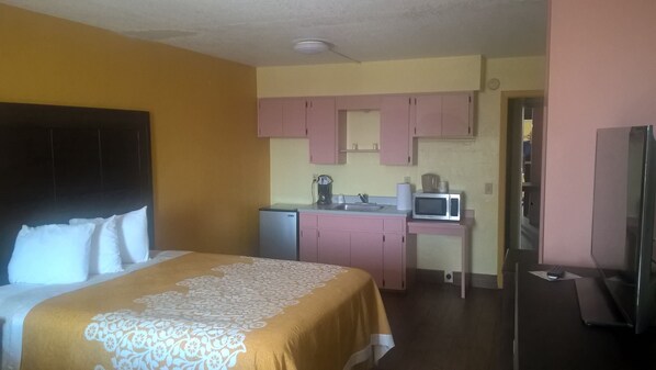 A hotel room with a bed, a kitchenette, and a television.