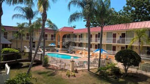 A hotel with a swimming pool surrounded by palm trees and a white fence.