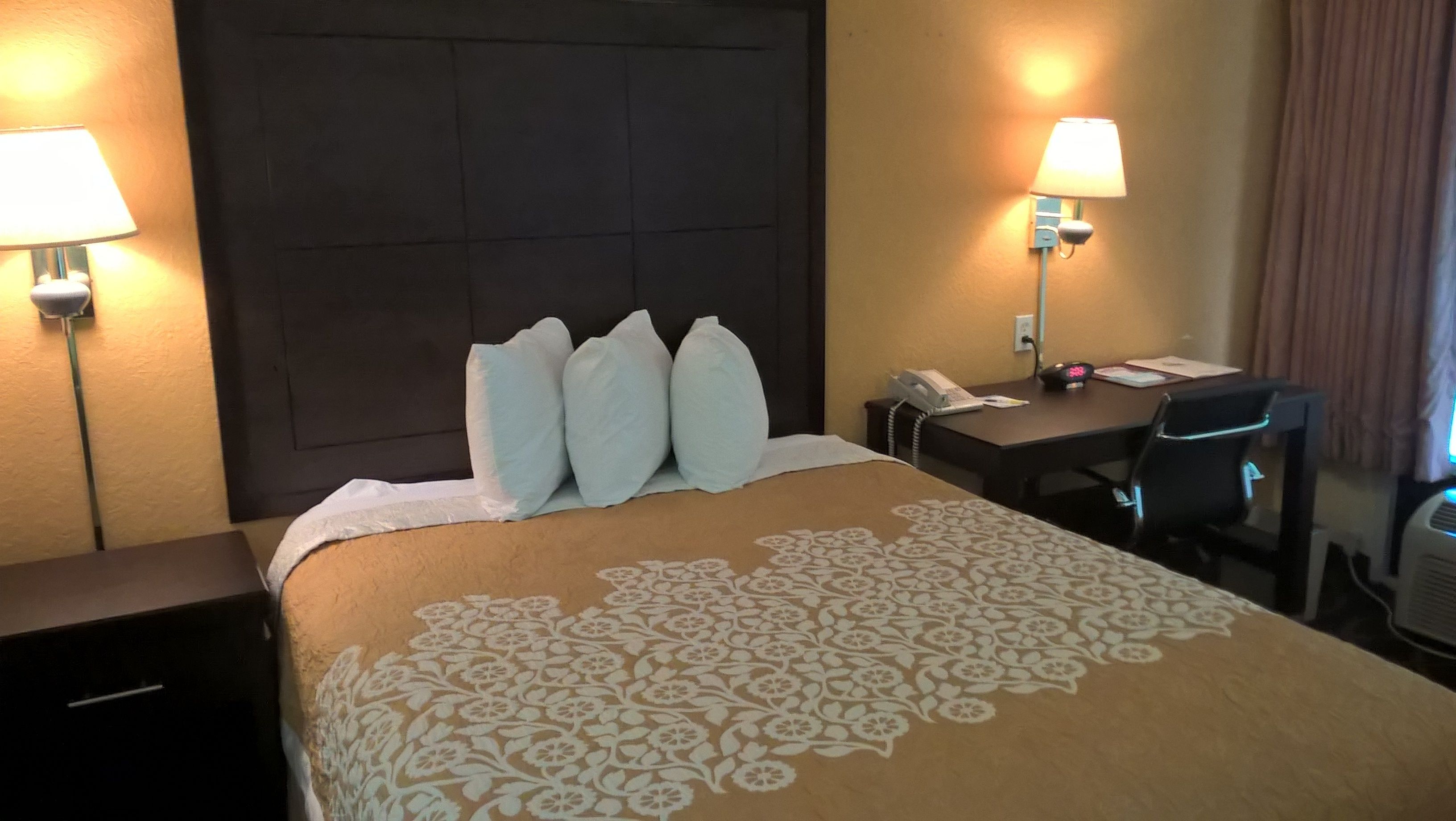A hotel room with a large bed, two bedside lamps, a desk with a telephone, and a chair.