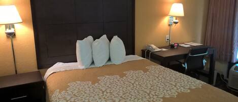 A hotel room with a large bed, two bedside lamps, a desk with a telephone, and a chair.