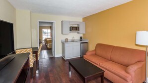 Un espace de vie compact comprenant un canapé, un téléviseur, une table à manger avec des chaises, une kitchenette équipée d’un four à micro-ondes et un petit coin repas.