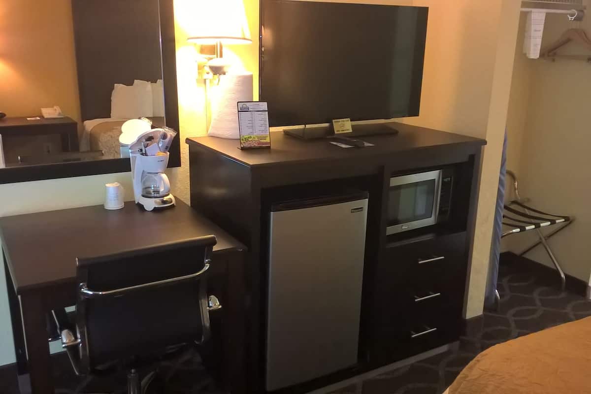 A compact hotel room with a desk, a refrigerator, a microwave, a television, and a chair.