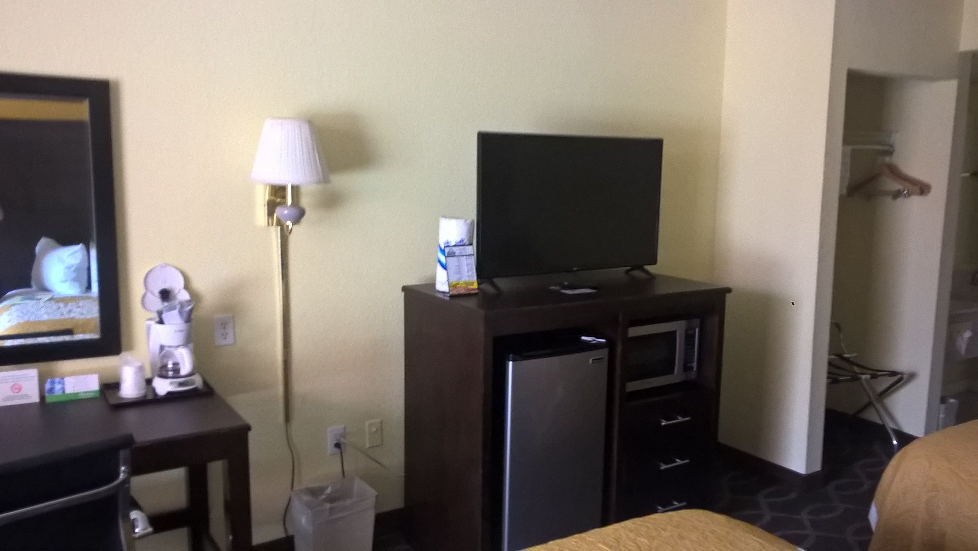 A hotel room with a TV on a cabinet, a lamp, a trash bin, and a bed.