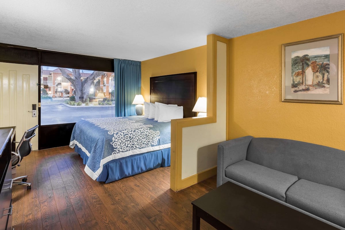 A hotel room with a bed, a desk, a chair, a sofa, and a painting on the wall.