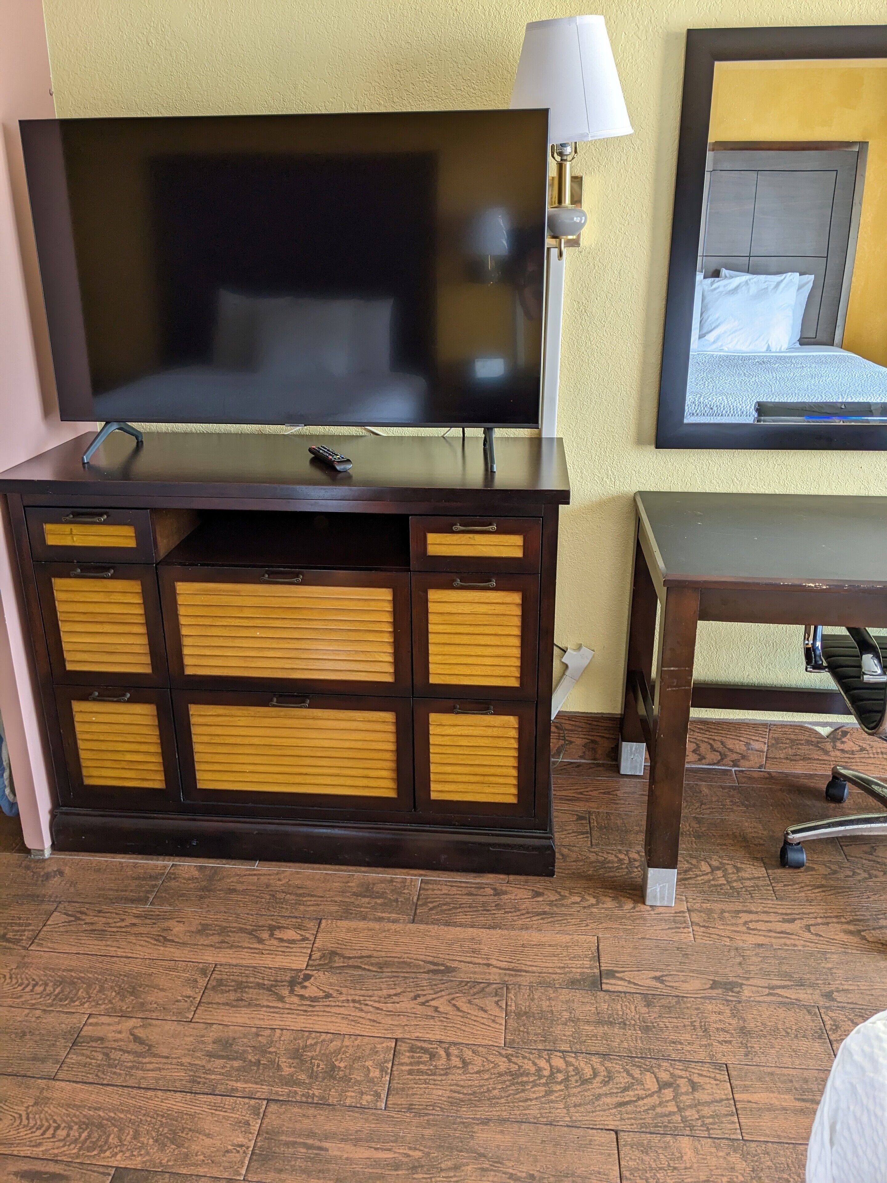Une chambre d’hôtel dotée d’un grand téléviseur à écran plat posé sur une console en bois foncé, d’une table de chevet avec une lampe et d’un lit avec une tête de lit et des oreillers.