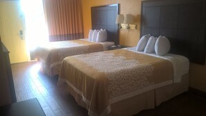 A hotel room with two beds, each with a headboard, a bedside table, and a lamp.