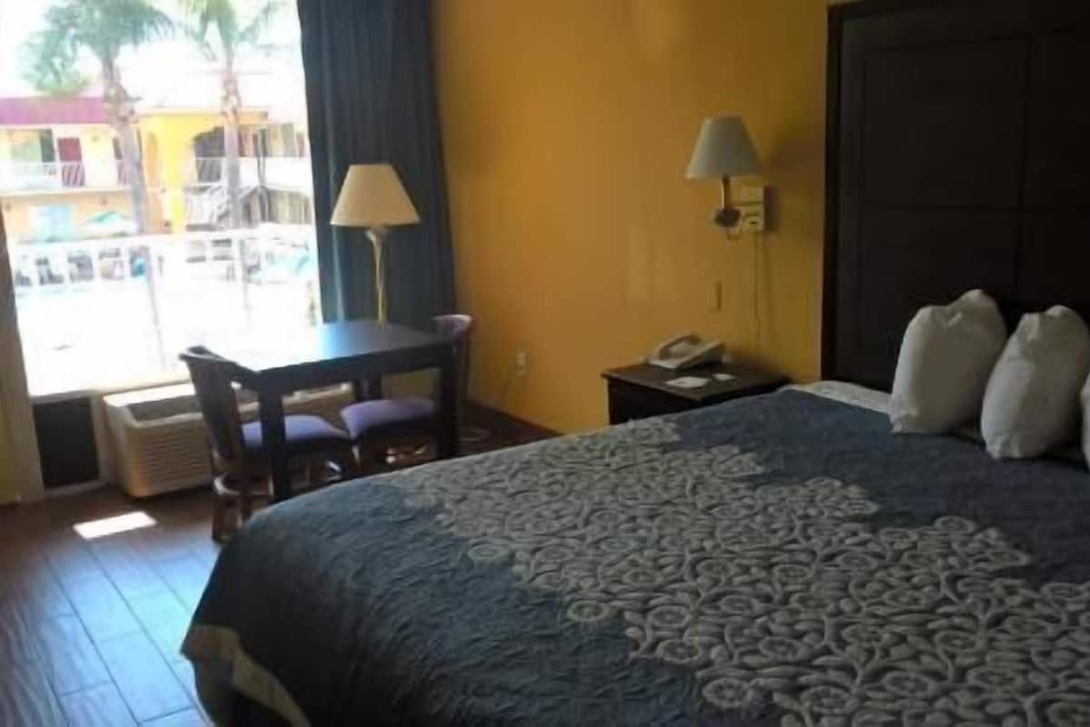A hotel room with a bed, a desk, a chair, a lamp, and a view of the outside.