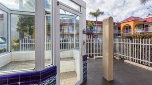 L’entrée d’un hôtel avec une porte en verre, une terrasse carrelée et une clôture blanche.