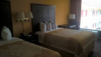 A hotel room with two beds, a nightstand with a lamp, a clock, and a window with curtains.