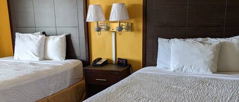 A hotel room with two beds, a nightstand with a lamp, and a phone.