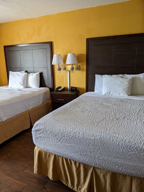 A hotel room with two beds, a nightstand with a lamp, and a phone.