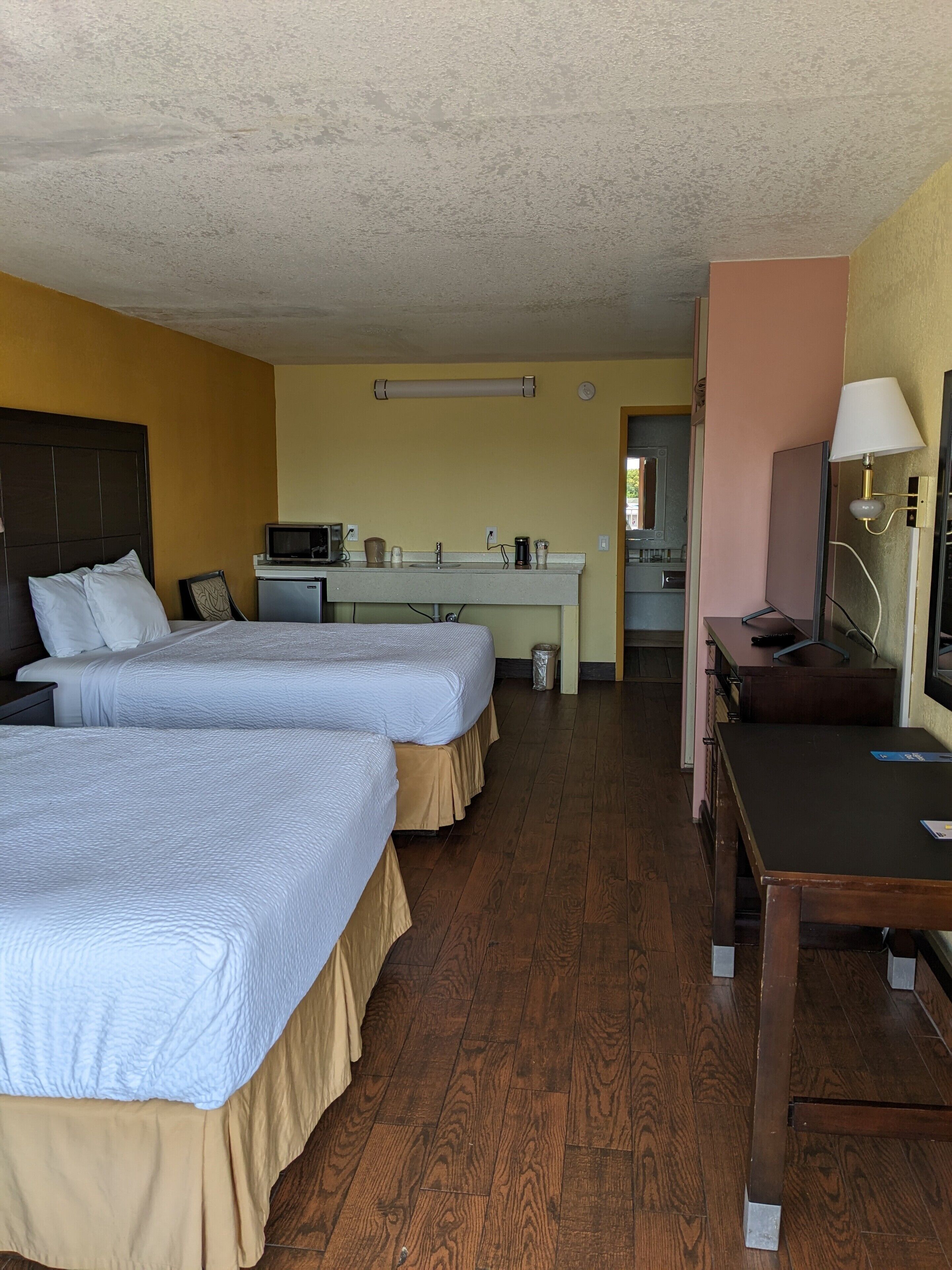 A hotel room with two beds, a kitchenette, a small dining table, and a TV.