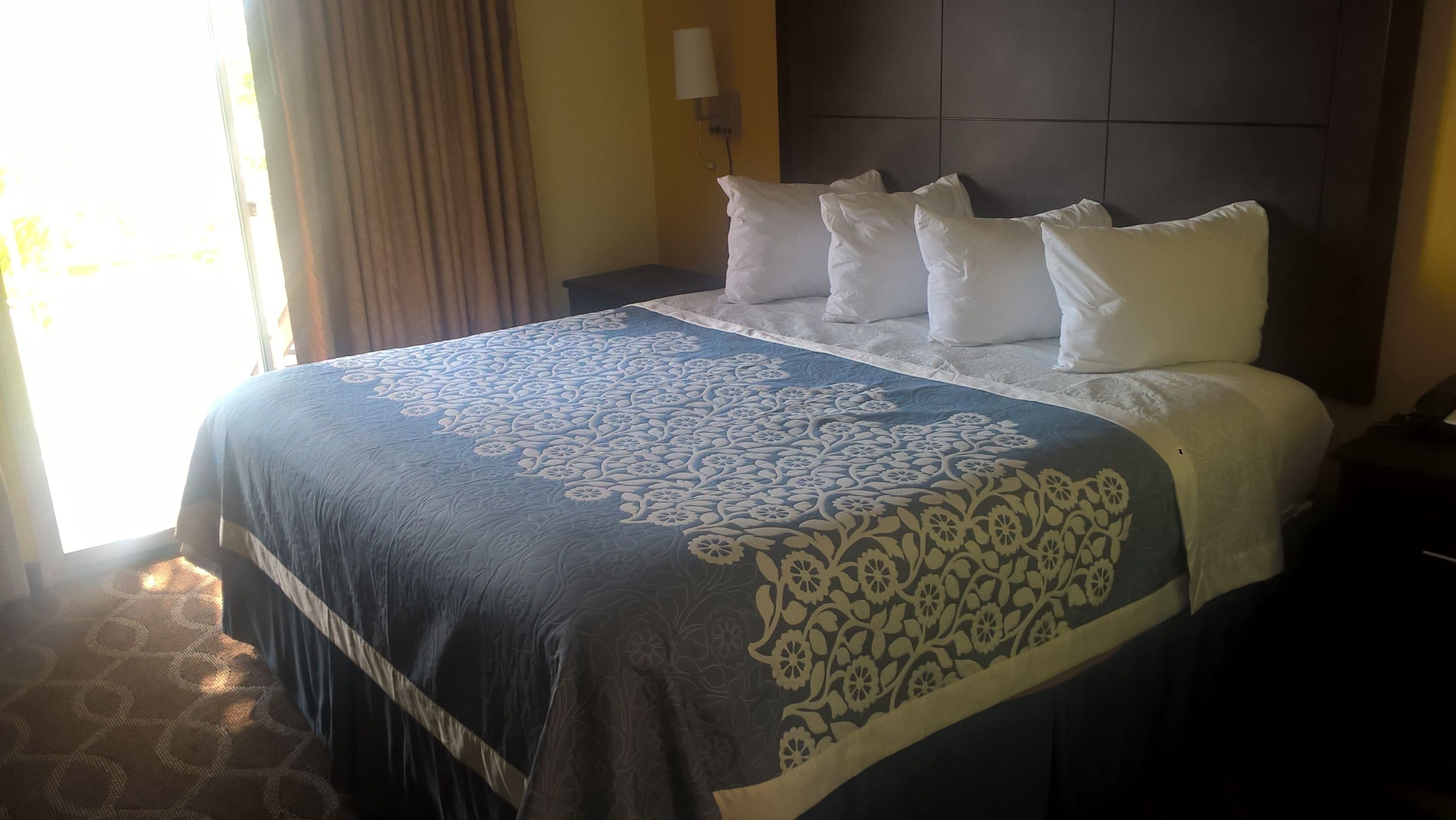 A hotel room with a large bed, a nightstand, a lamp, and a window with curtains.
