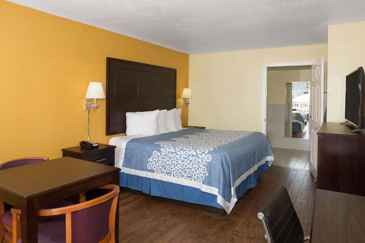 A hotel room with a bed, bedside tables, a desk, a chair, a TV, and a door leading to another room.