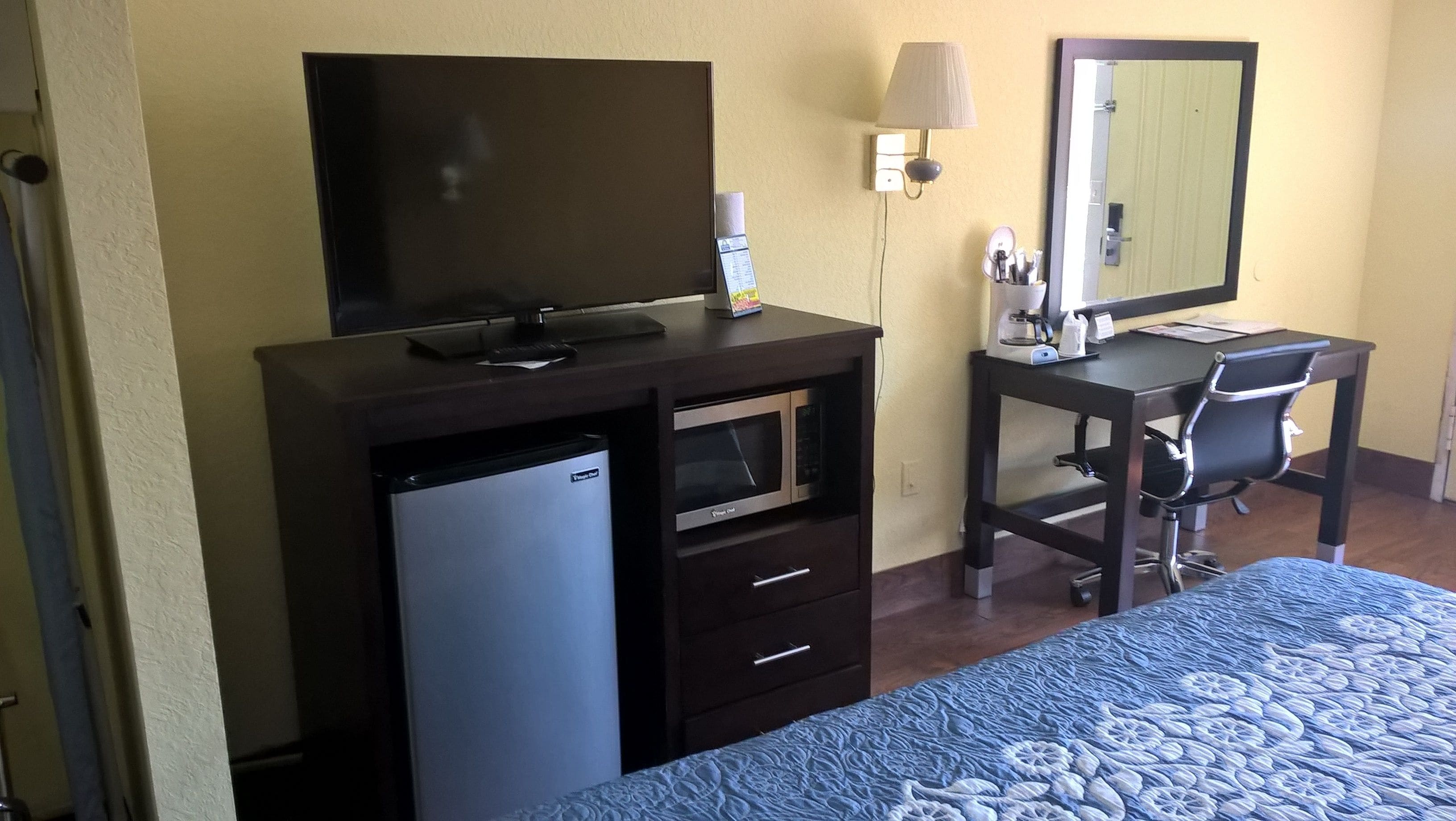 Een hotelkamer met een bed, een bureau met stoel, een televisie, een magnetron en een koelkast.