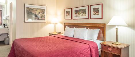 Habitación de hotel con una cama grande, dos mesitas de noche con lámparas, un aparador de madera y tres cuadros enmarcados en la pared.