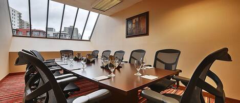 A conference room with a long table, multiple chairs, and a city view through large windows.