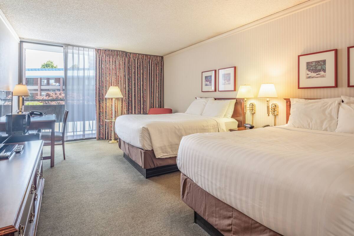 Une chambre d’hôtel avec deux lits, un bureau avec une chaise, une lampe et une vue sur l’extérieur.
