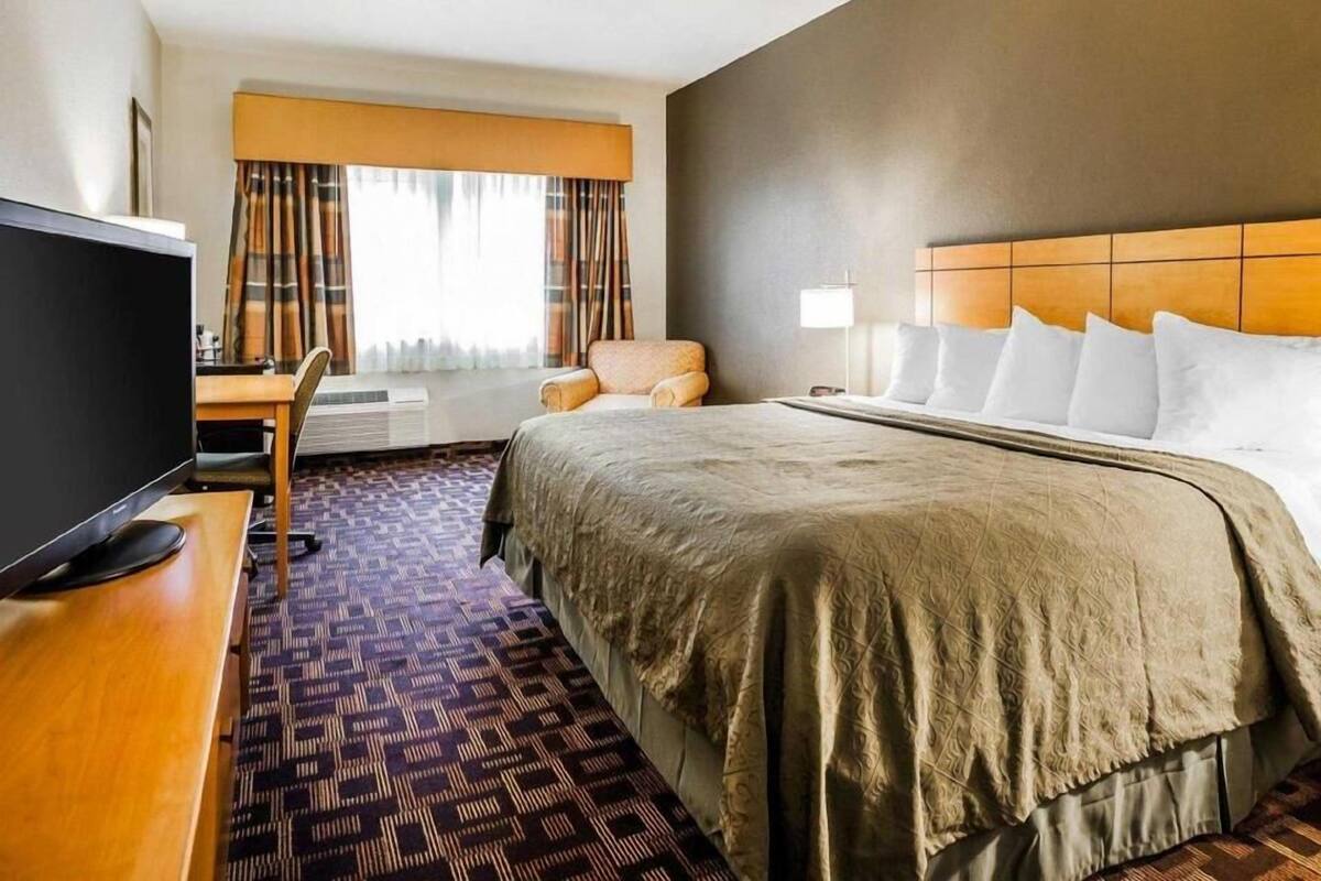 A hotel room with a bed, a desk with a TV, a chair, and a window with curtains.