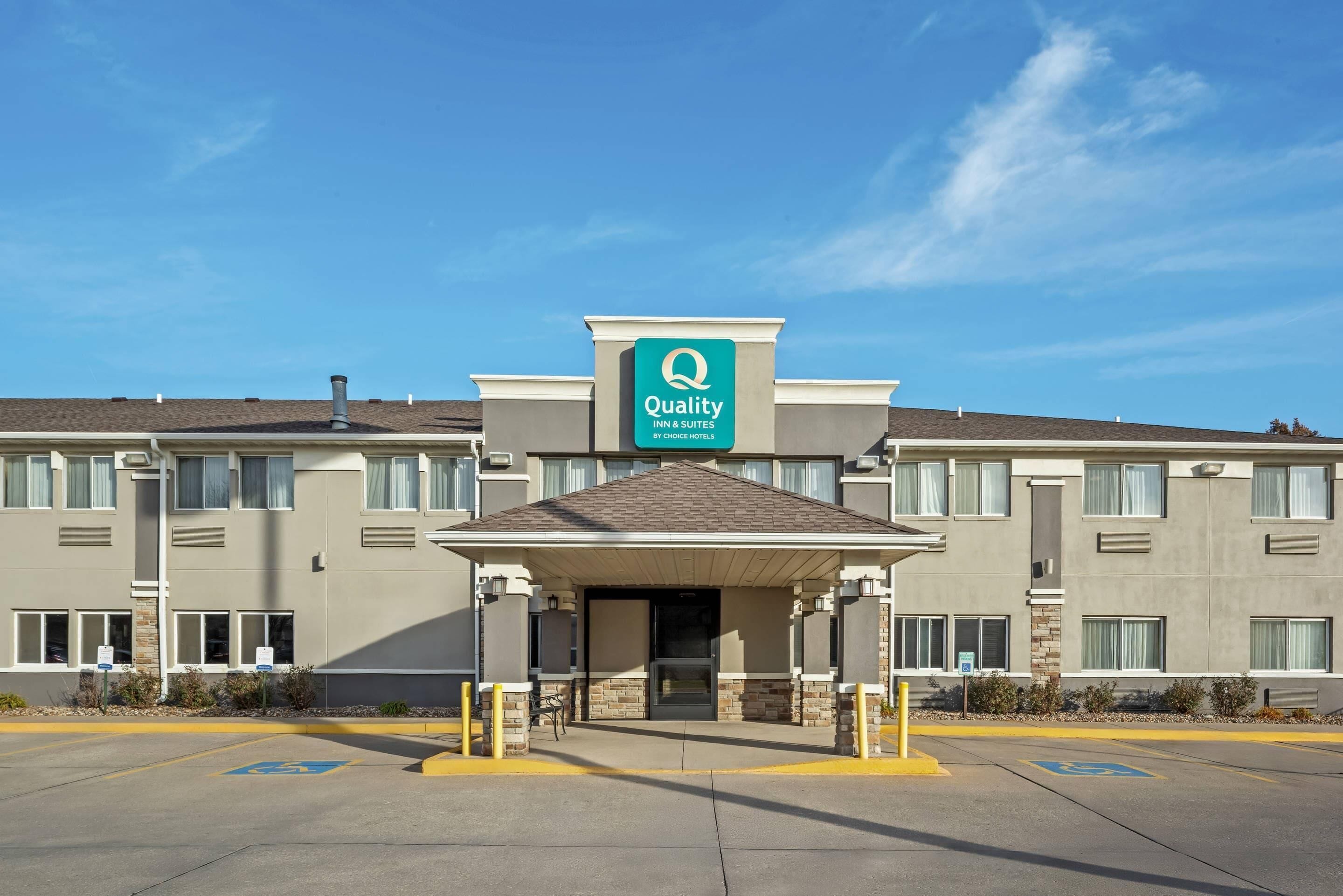 A Quality Inn & Suites by Choice Hotel with a covered entrance, handicap-accessible parking, and a clear blue sky.