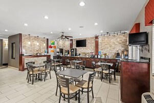Un restaurante con pared de piedra, varias mesas, sillas, una barra y un televisor.