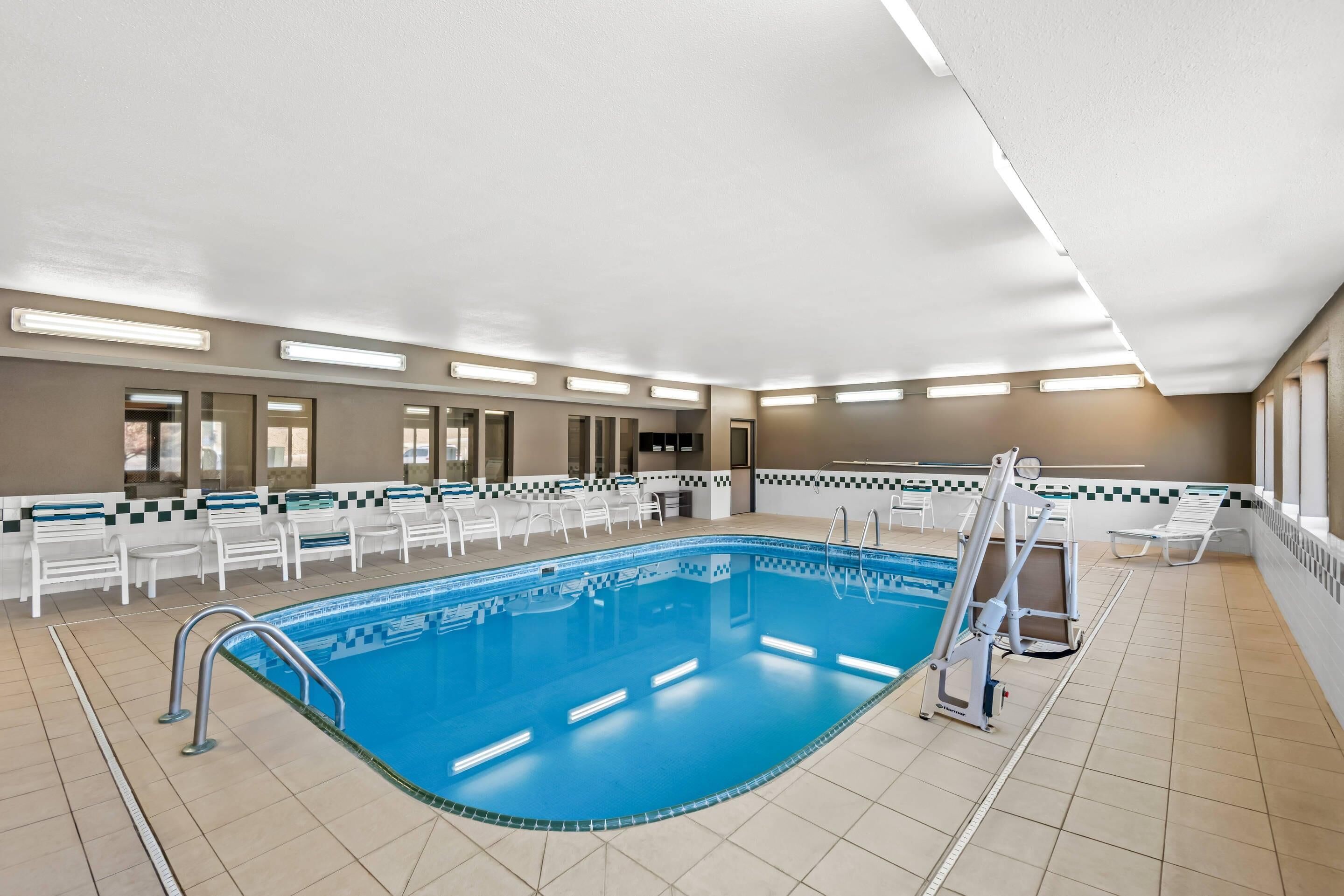 Une grande piscine intérieure dotée d’un plongeoir, entourée de chaises longues et ornée d’un motif mural à carreaux.