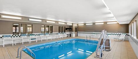 Una amplia piscina cubierta con un trampolín, rodeada de sillones de descanso y un patrón de pared a cuadros.