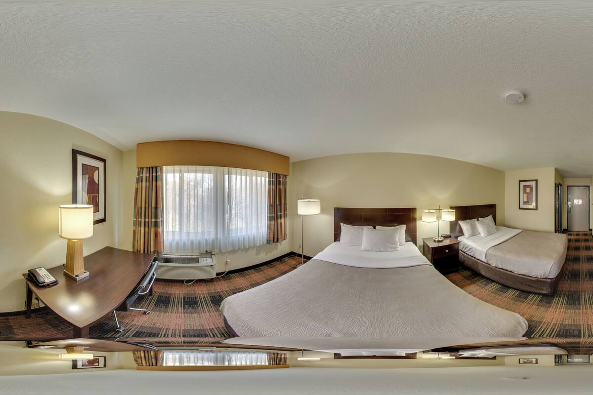 A hotel room with a large bed, a smaller bed, a desk, a TV, and a window with curtains.
